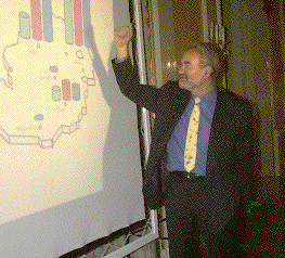 Robert Trappl speaking in front of a projected slide showing a map of Austria with various bar graphs superimposed
